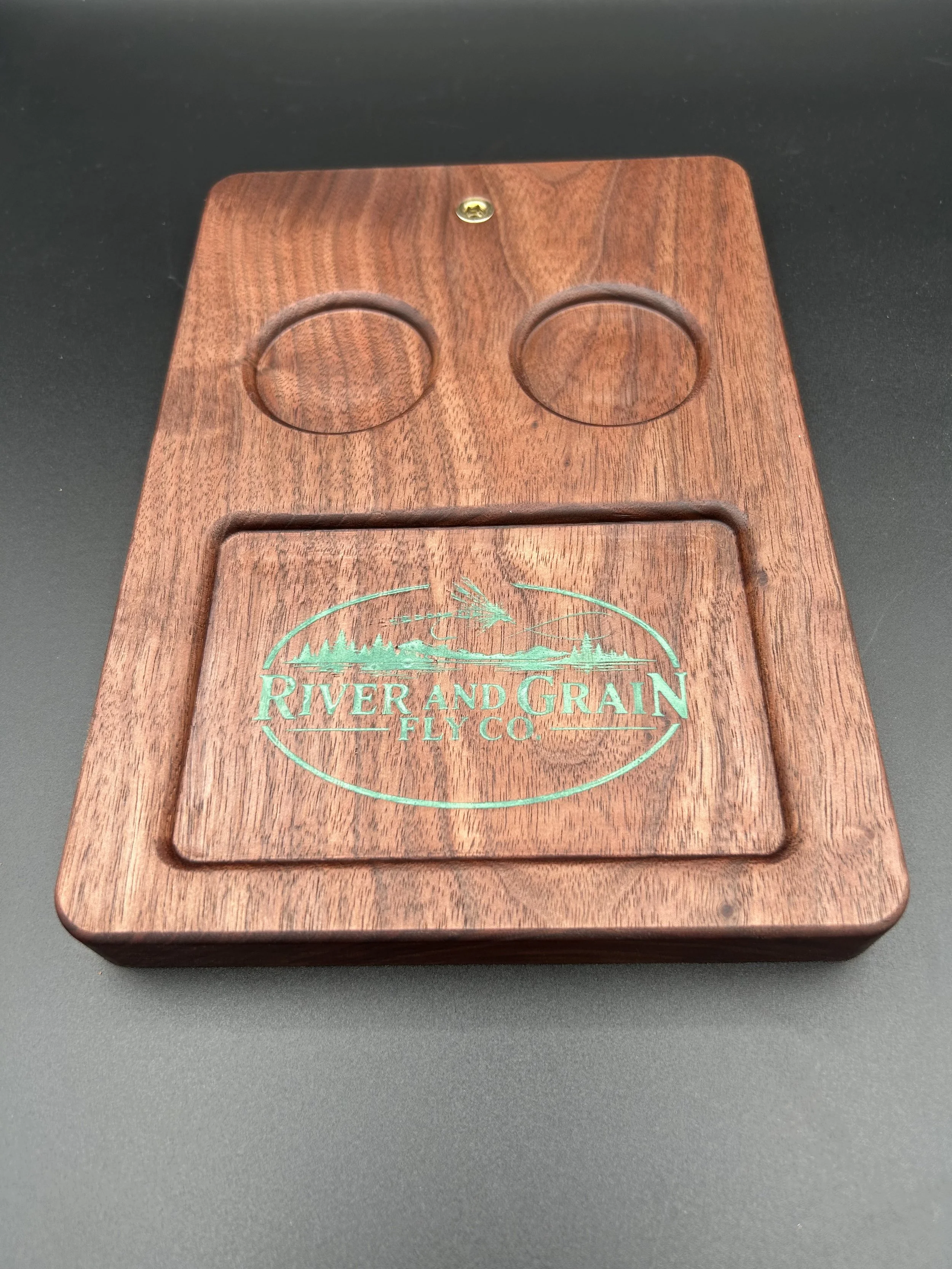 A wooden fly box with a natural finish, featuring a carved mountain and forest scene with the words 'River and Grain Fly Co.' in green.