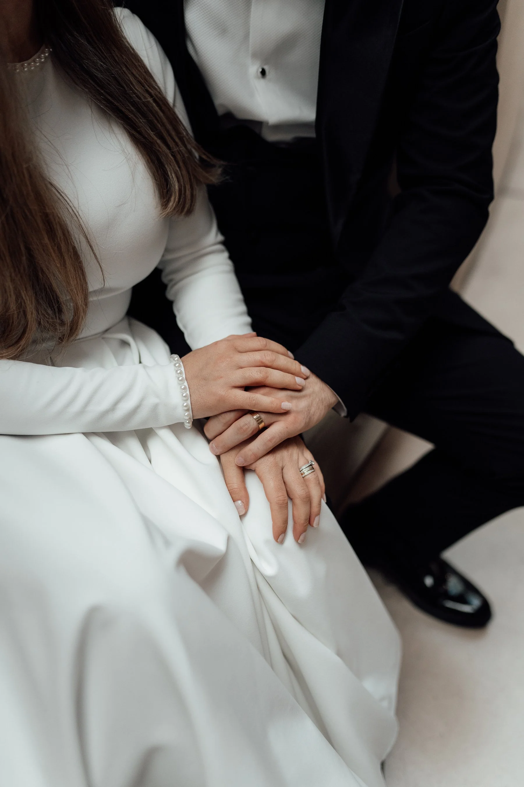 Close-up of a bride in a white dress and a groom in a black suit holding hands during a wedding ceremony.