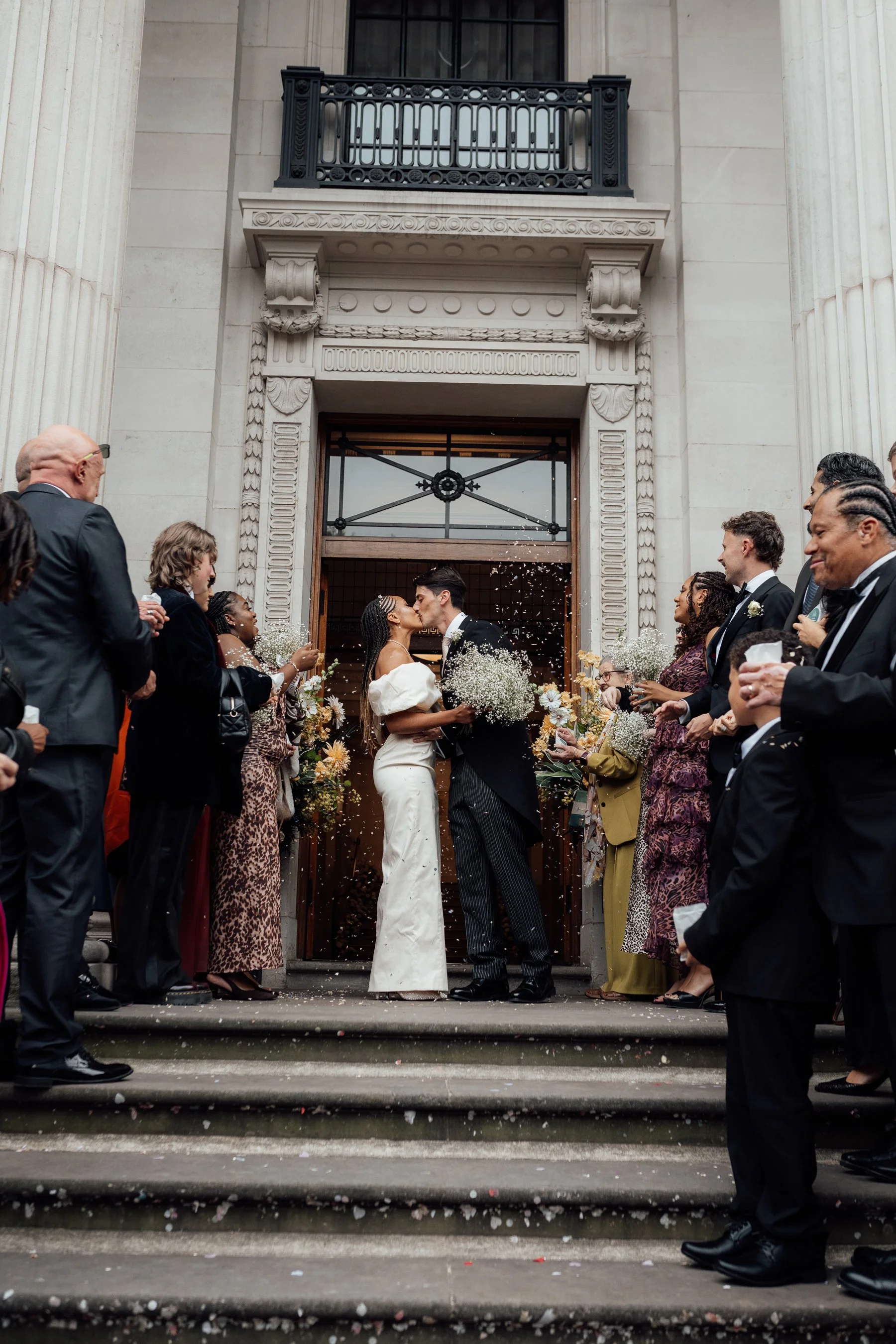 A wedding ceremony with a bride and groom kissing in front of a crowd outside a building.