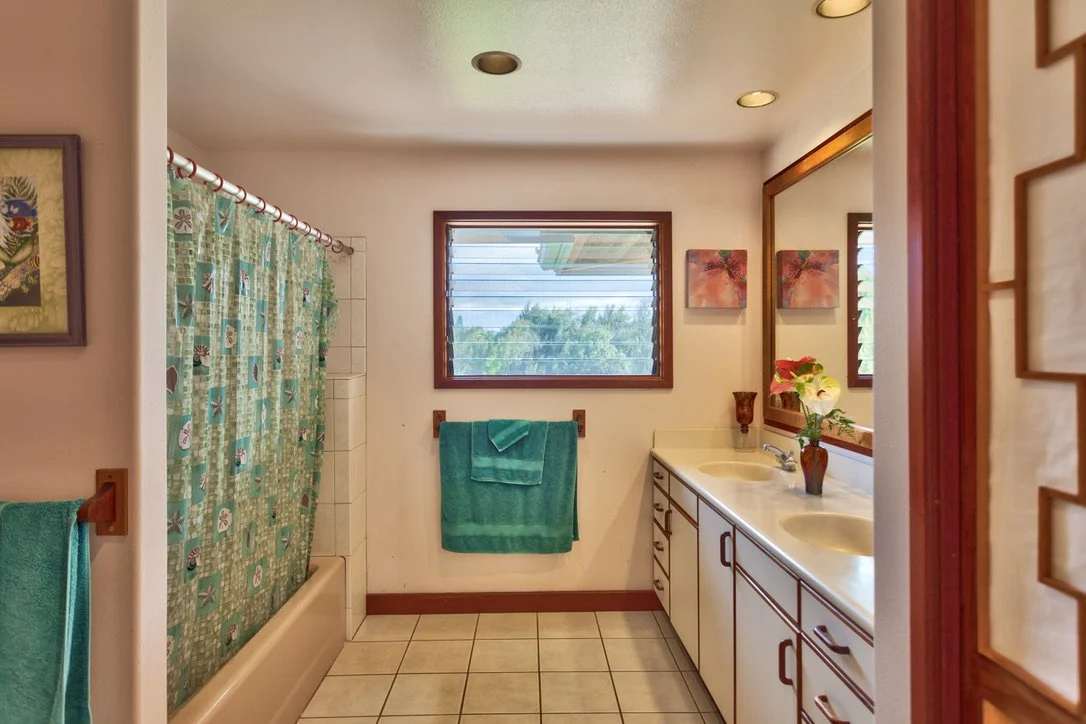 A bathroom with a bathtub and shower on the left, teal towels, a window with a view of trees, a double sink vanity with a large mirror on the right, and decorative wall art.