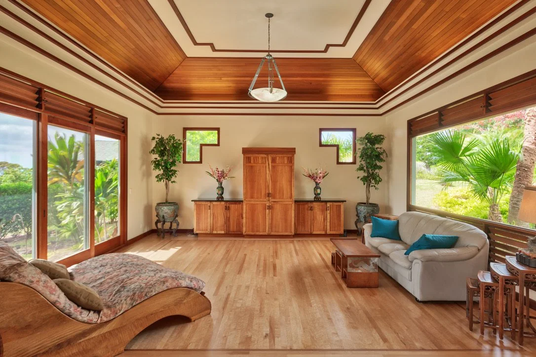 Living room with wooden ceiling, large windows, a white sofa with blue pillows, a wooden coffee table, and houseplants.
