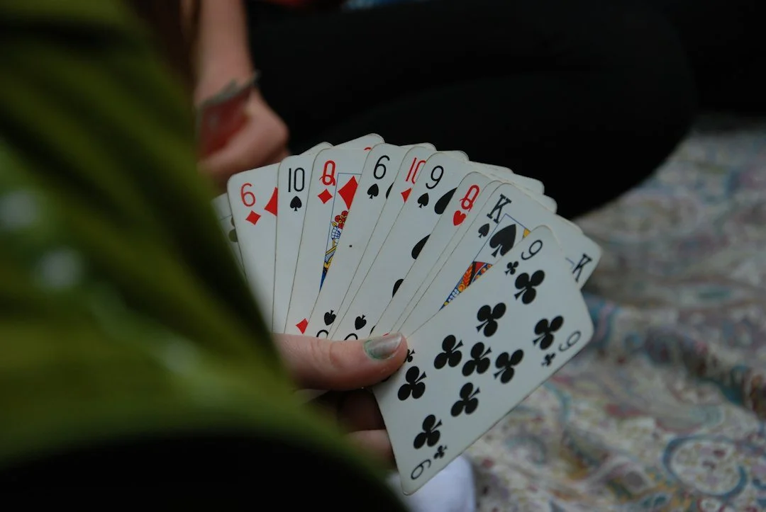 A person holding a fan of playing cards, including six of diamonds, ten of spades, queen of diamonds, six of spades, ten of diamonds, nine of spades, queen of hearts, king of spades, nine of clubs, and king of clubs, with a blurred background.