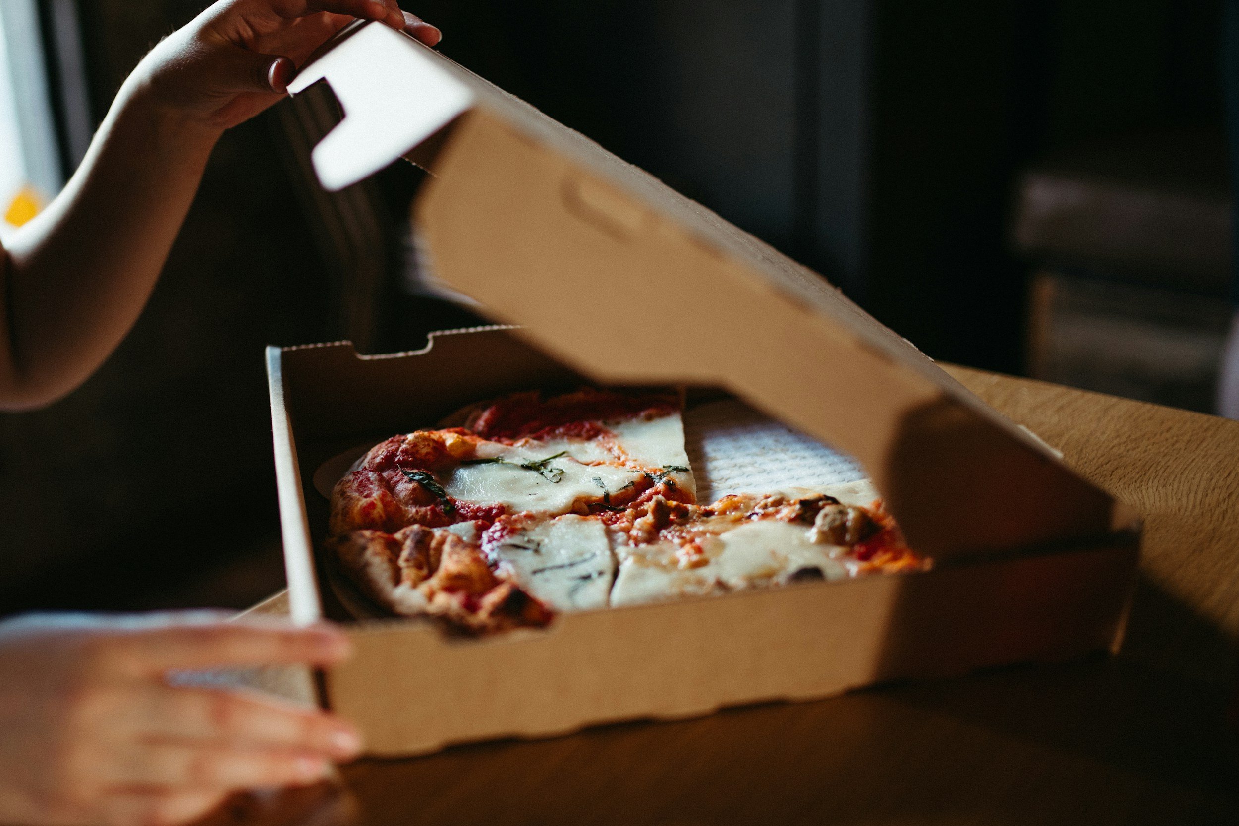 Close-up of a hand opening a pizza box with two slices of pizza inside.