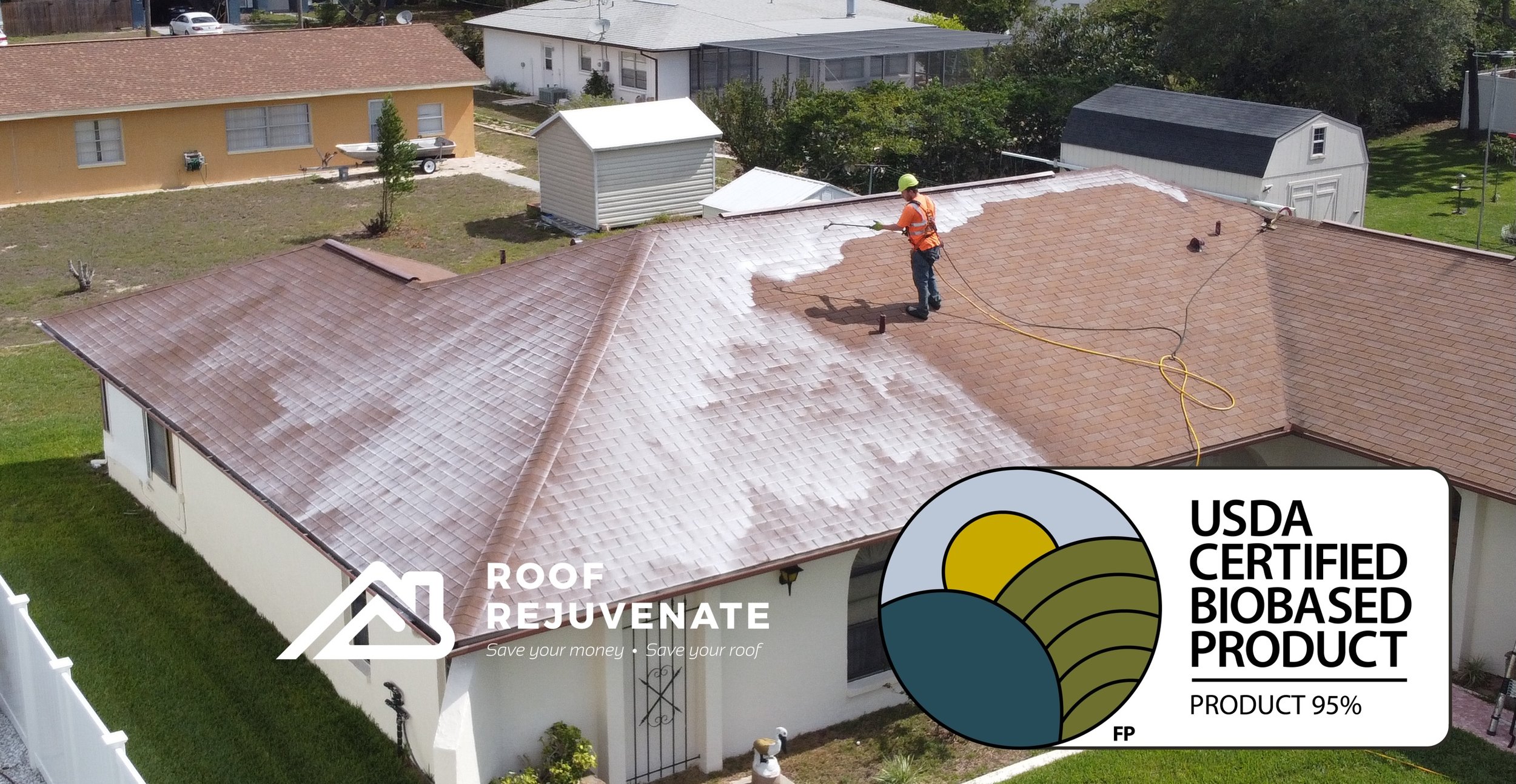 A worker wearing a safety helmet and an orange vest is power washing the roof of a house with tan and brown shingles. The house has a white exterior, and neighboring houses and green lawns are visible in the background.