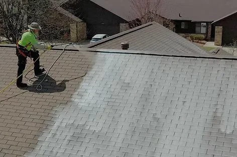 Person using a pressure washer to clean a roof with a large portion covered in white cleaning solution.