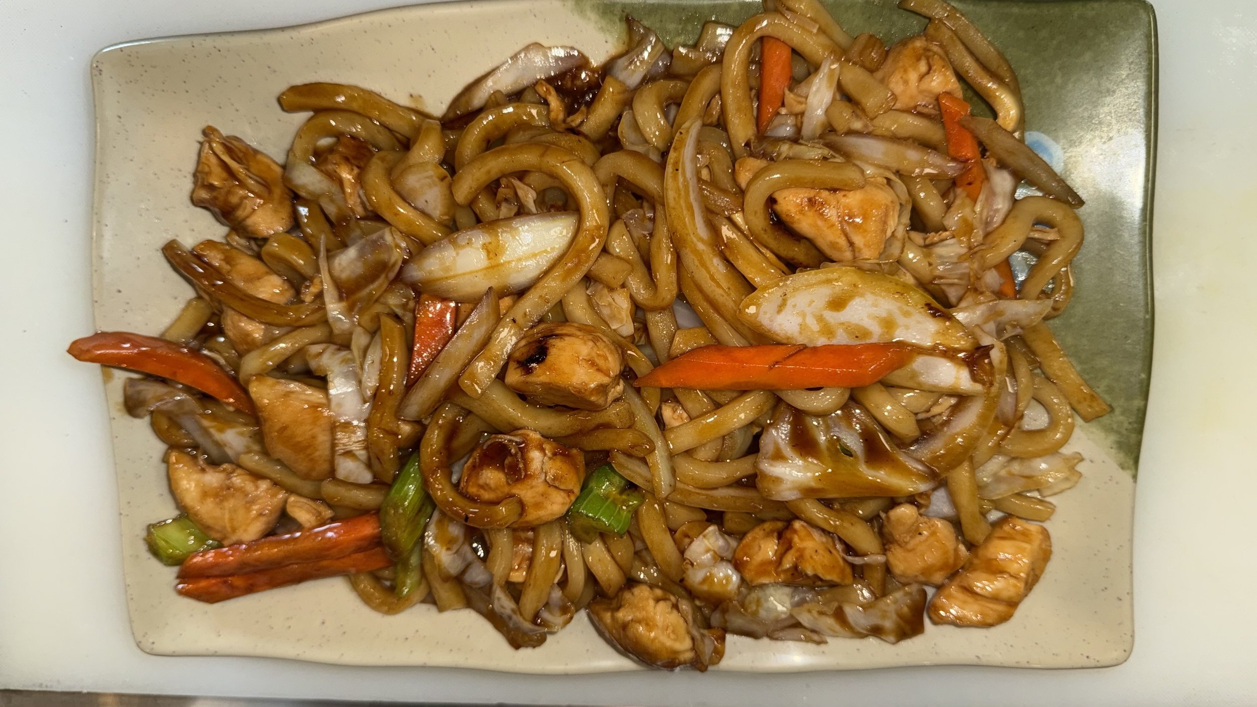 Plate of stir-fried noodles with chicken, vegetables, and sauce.