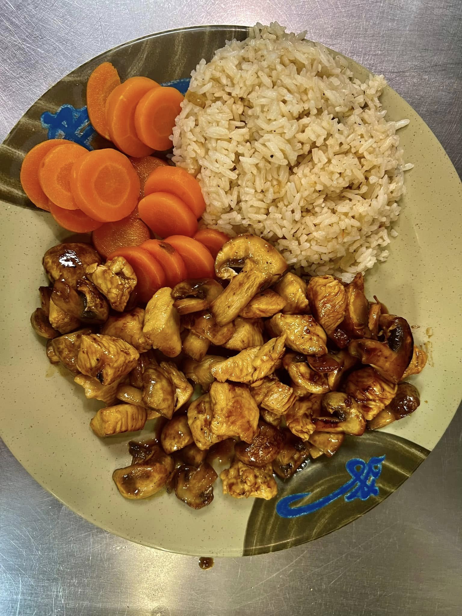 A plate of cooked rice, sliced carrots, sautéed mushrooms, and pieces of chicken stir-fried in sauce.
