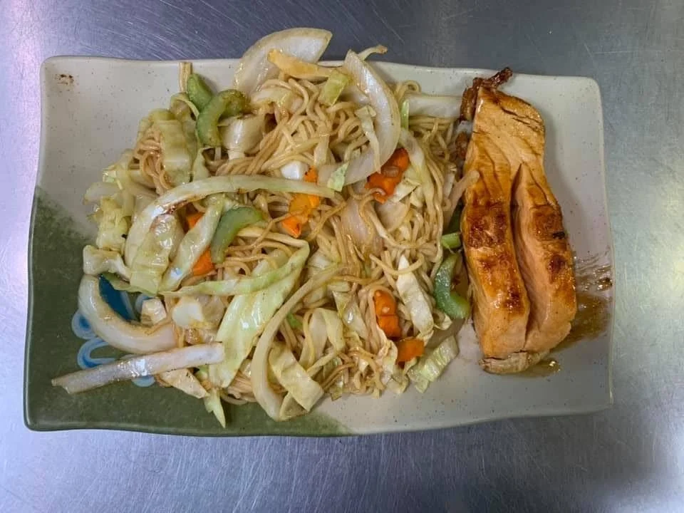 A plate with stir-fried noodles and vegetables along with two pieces of cooked salmon.