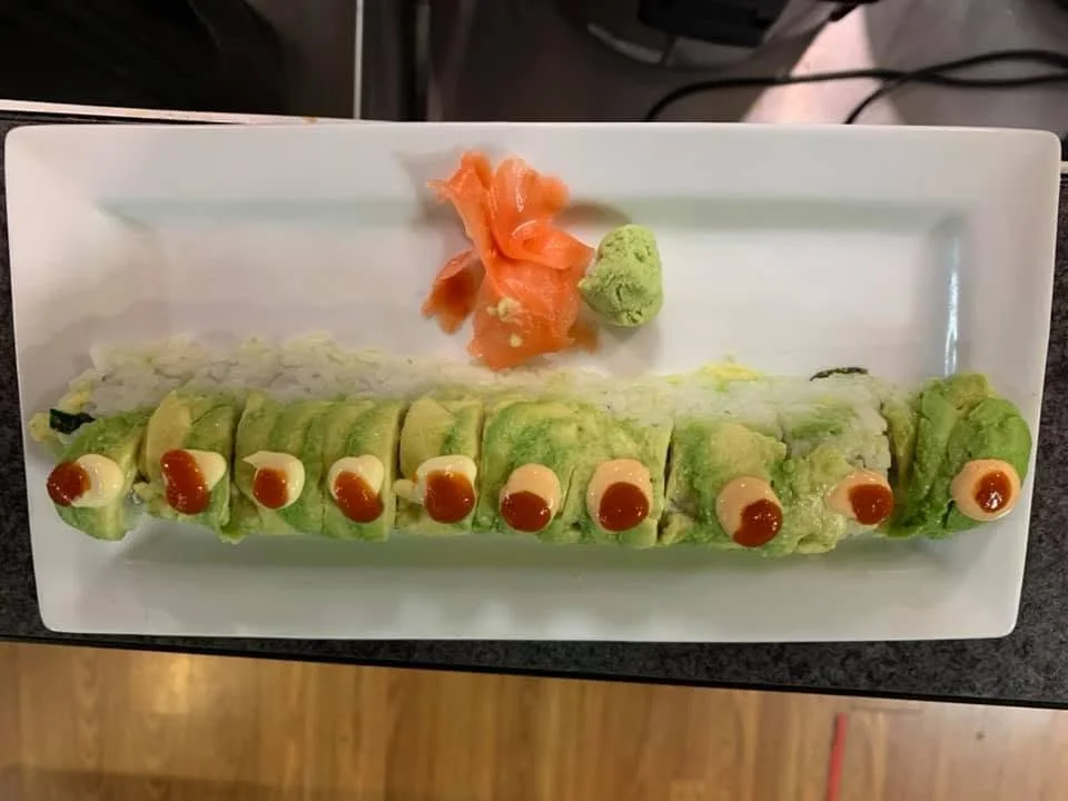 A plate of chopped avocado sushi rolls topped with mayonnaise and hot sauce, with slices of ginger, wasabi, and a small pile of pickled ginger on the side.