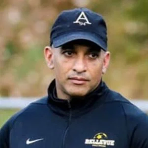 Man wearing navy baseball cap with a white letter 'A' and navy sports jacket with logos