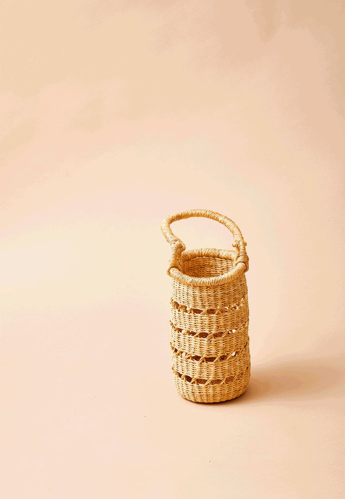 A tall woven basket with a handle, made from natural fibers, placed on a neutral background.