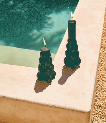 Two black candles with flames on a white surface near a swimming pool.