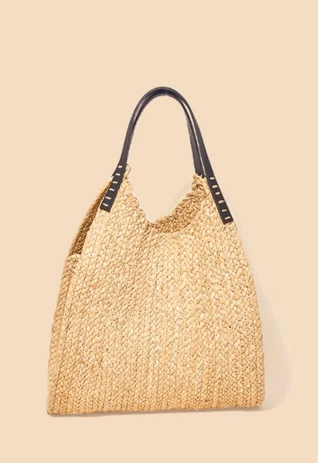 A woven beige tote bag with black handle straps hanging on a plain wall.