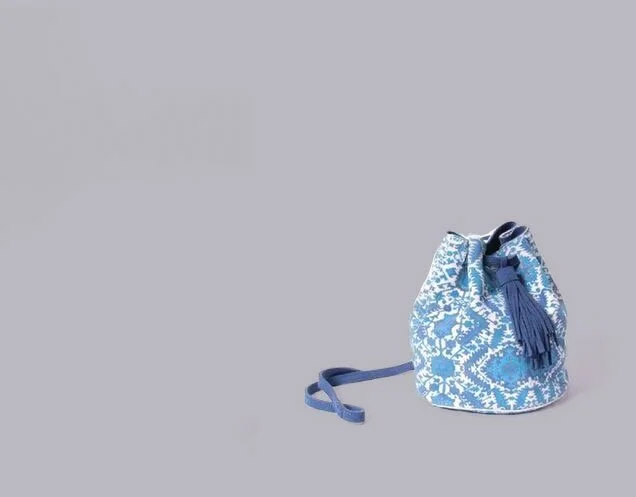 Blue and white patterned bucket bag with a tassel, isolated on a gray background.