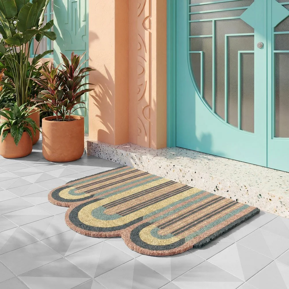 A colorful striped doormat in front of a turquoise door surrounded by potted plants on a tiled porch.