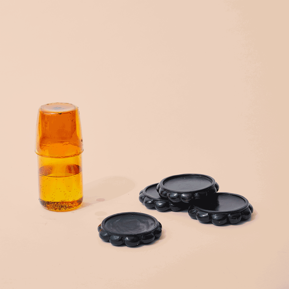 A stack of two amber glass bottles and three black ceramic coasters on a beige background.