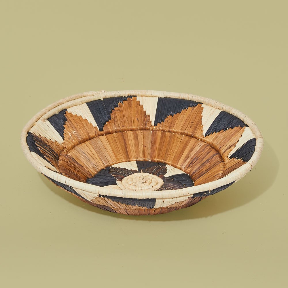 Decorative woven basket with black, white, and brown geometric patterns, placed on a pale green surface.