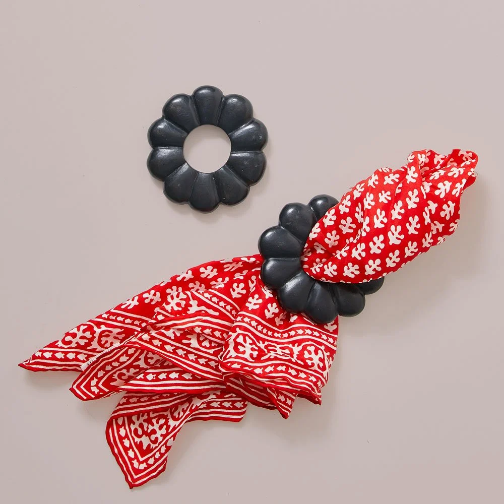 A black scrunchie and a black hair clip on a beige surface, with red and white patterned bandanas. The bandanas are folded and tied, with one partially tucked under the scrunchie.