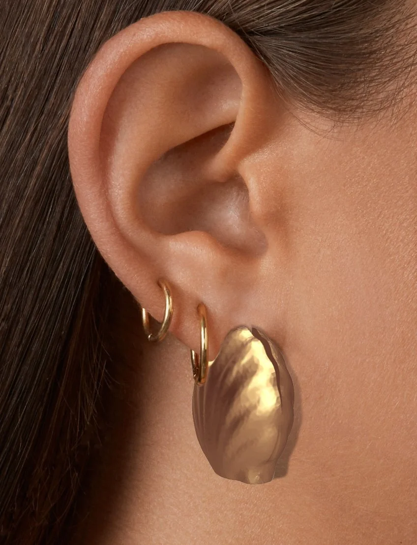 Close-up of a person's ear with three gold earrings and a large gold-colored earring attached to the earlobe.