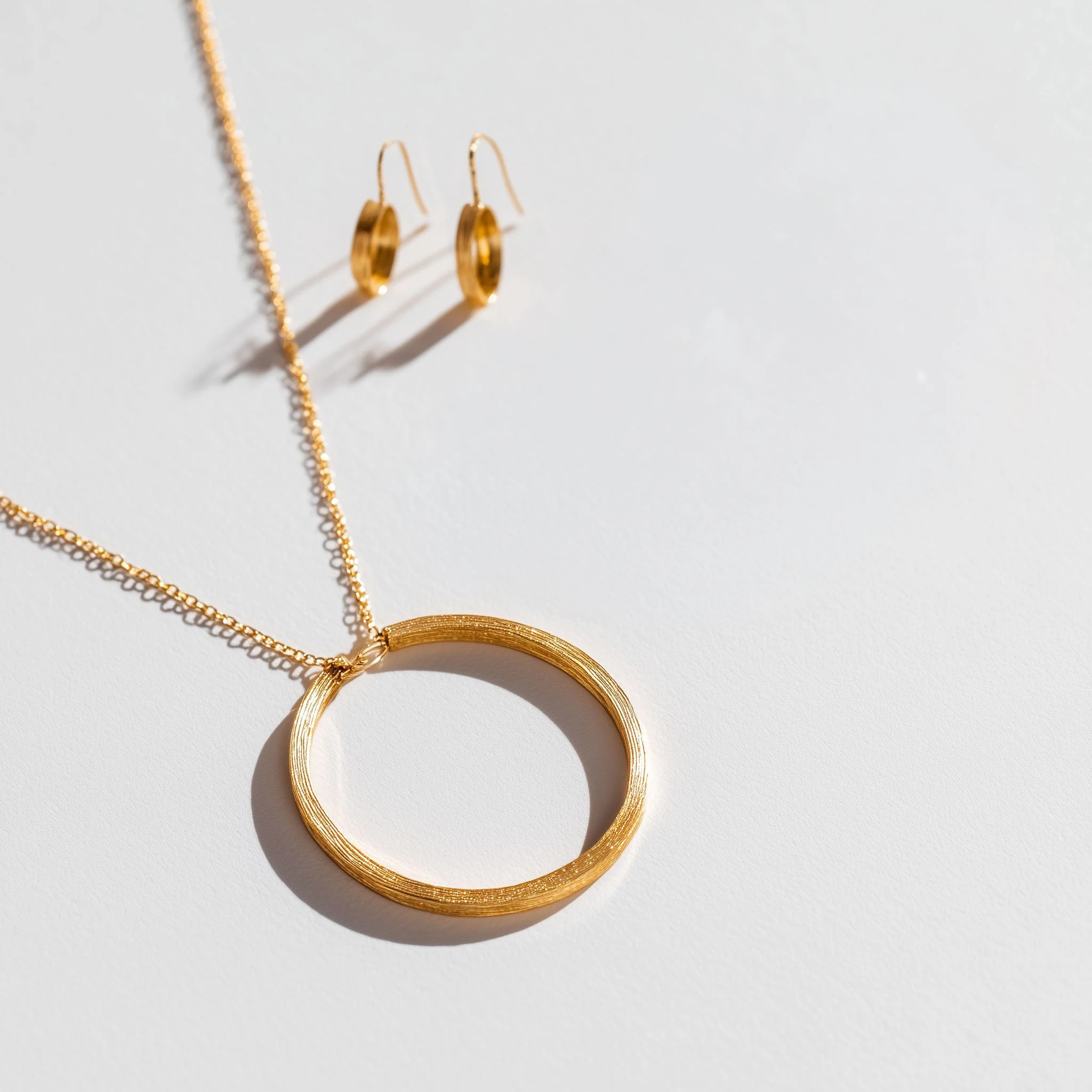 Close-up of gold jewelry including a pair of hoop earrings and a necklace on a white surface.