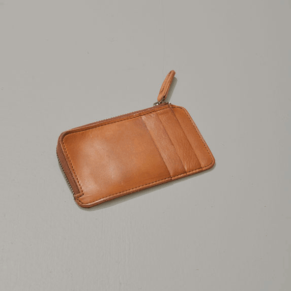 A brown leather zippered wallet with a keychain zipper pull resting on a light gray surface.
