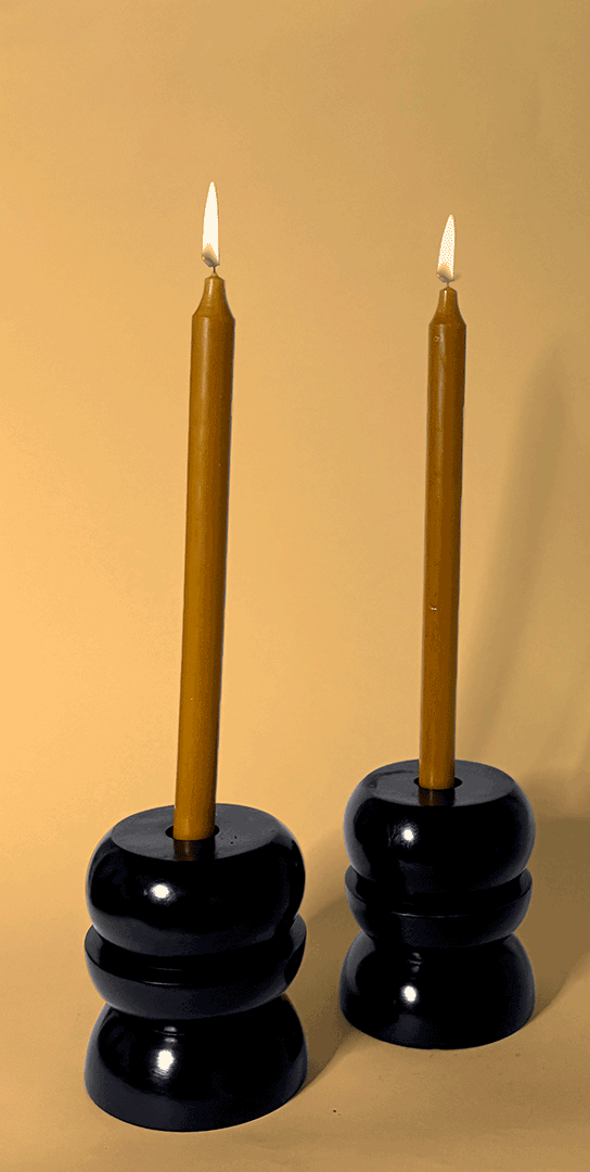 Two black candle holders with gold candles, each with a lit candle on top, against a beige background.