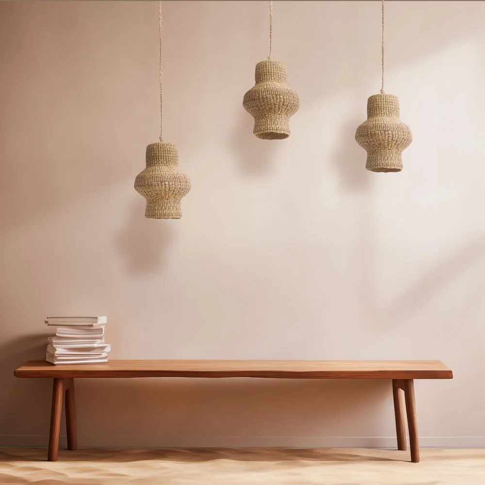 A minimalist decor with three woven pendant lights hanging above a wooden bench, and a small stack of white books on the bench.