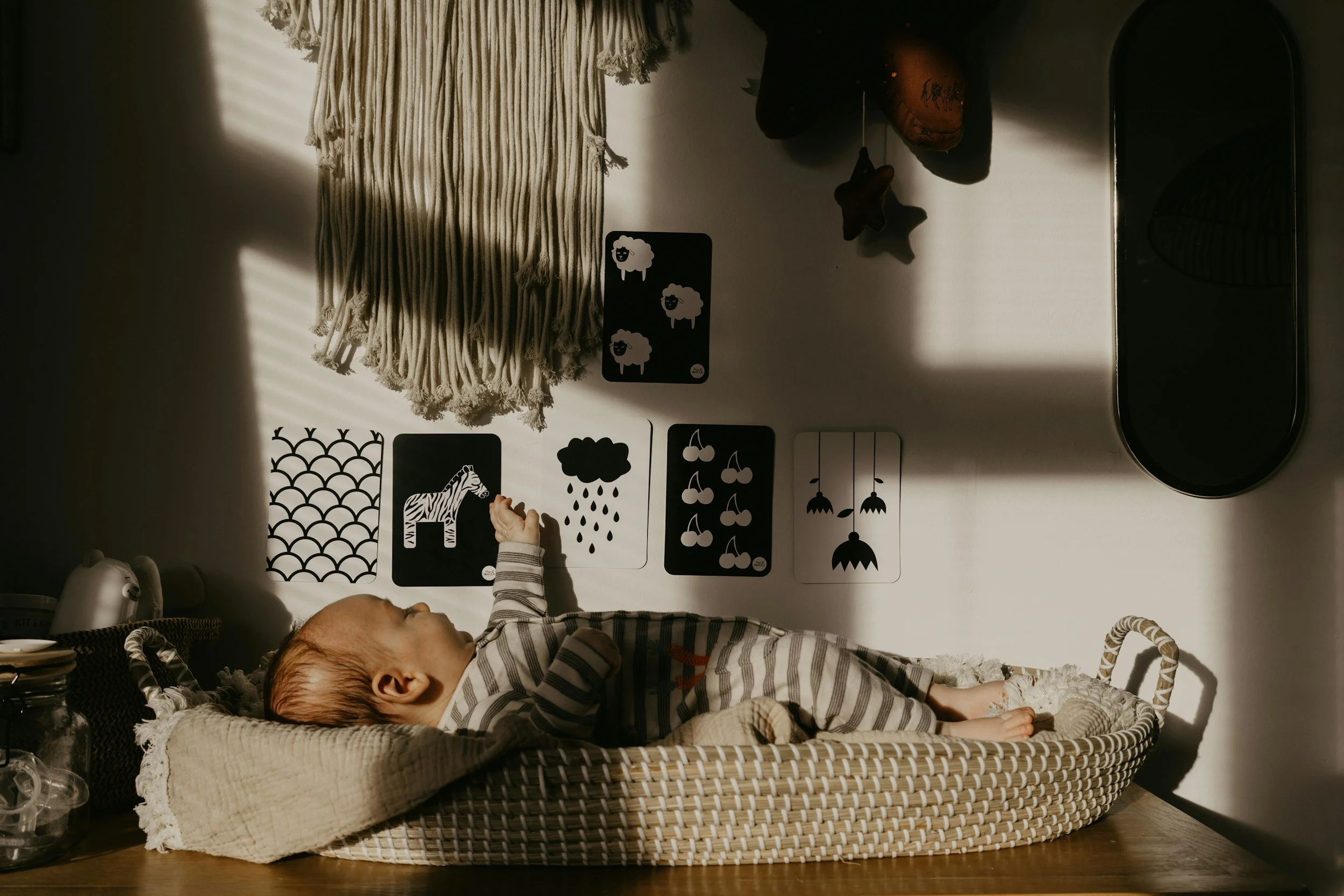 infant baby laying in basket playing with black and white pictures on wall