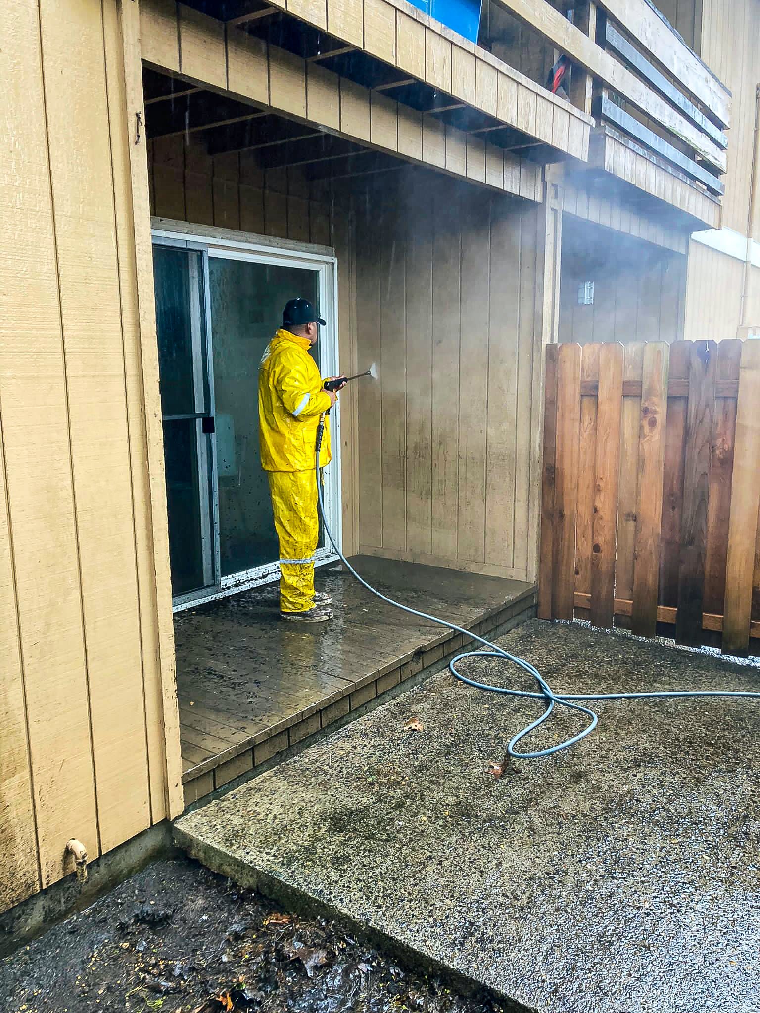 A person in a yellow suit power-washing the side of an apartment complex unit.