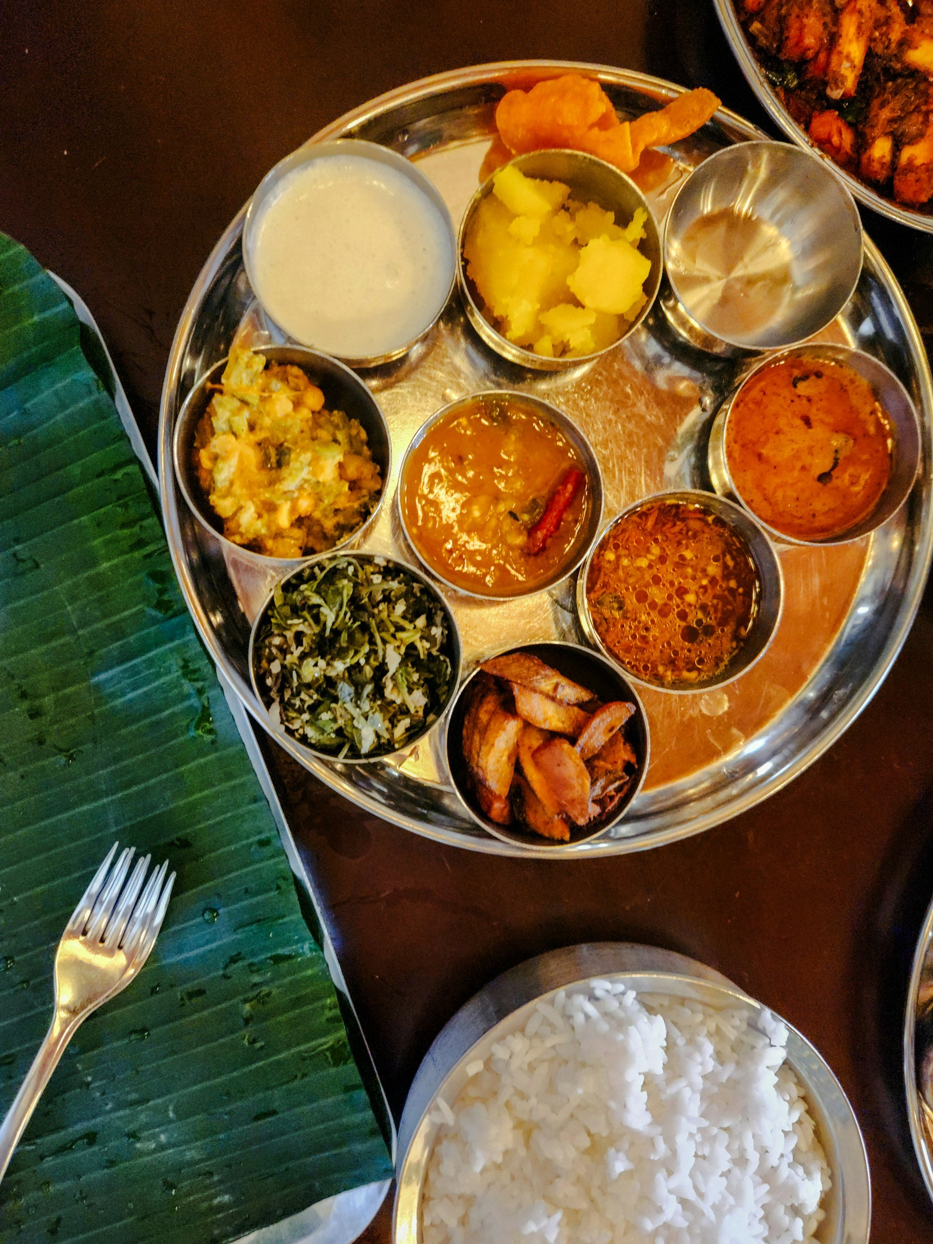 A traditional Indian thali meal with various side dishes, vegetables, dal, rice, and condiments served on a stainless steel platter.