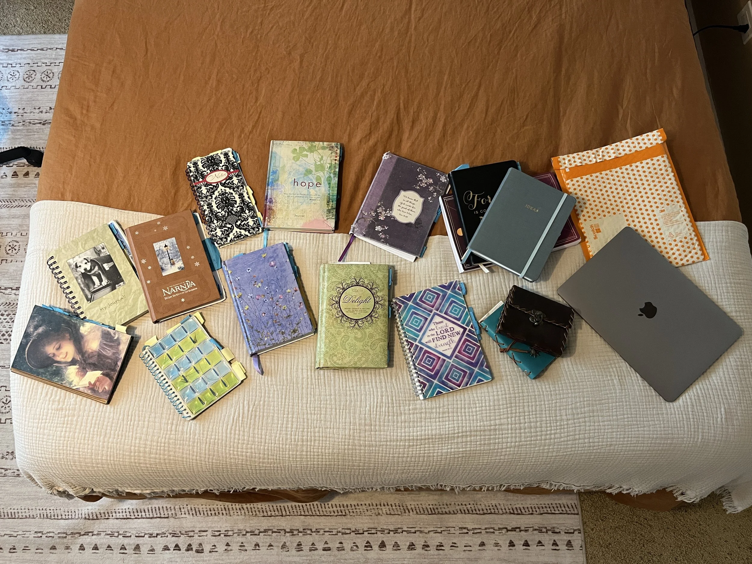 A collection of notebooks, journals, and notebooks spread out on a beige cushioned surface and a brown table.