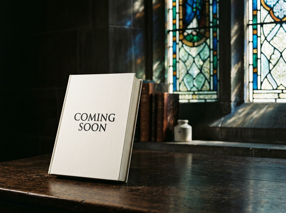 A white book with the words 'COMING SOON' on the cover, placed on a wooden table inside a room with stained glass windows and a few books and decorative items in the background.