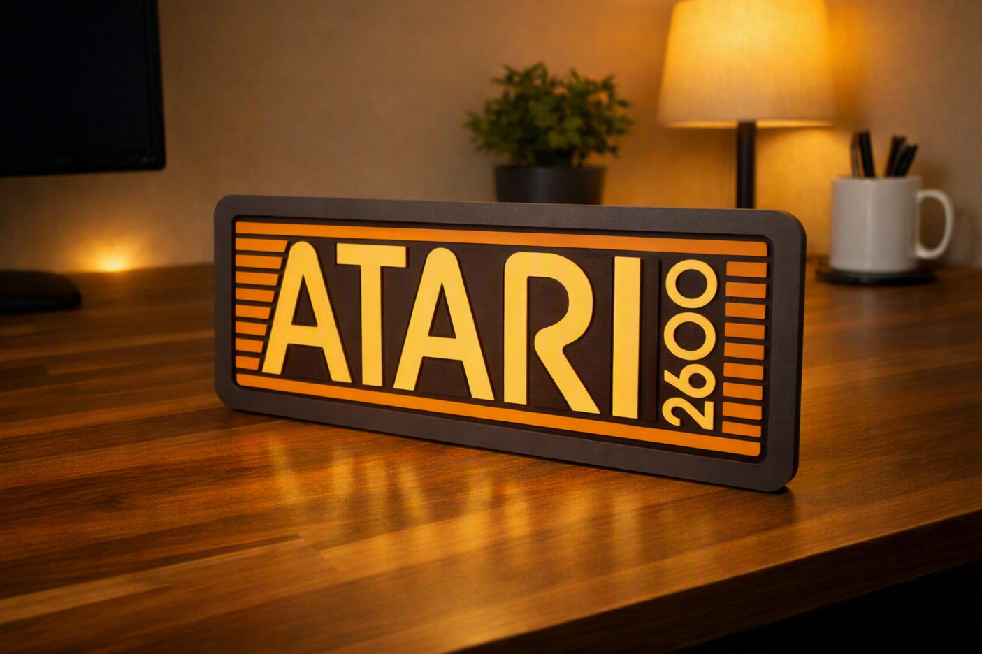 Illuminated Atari sign on wooden desk with a lamp, plant, and pen holder in the background.