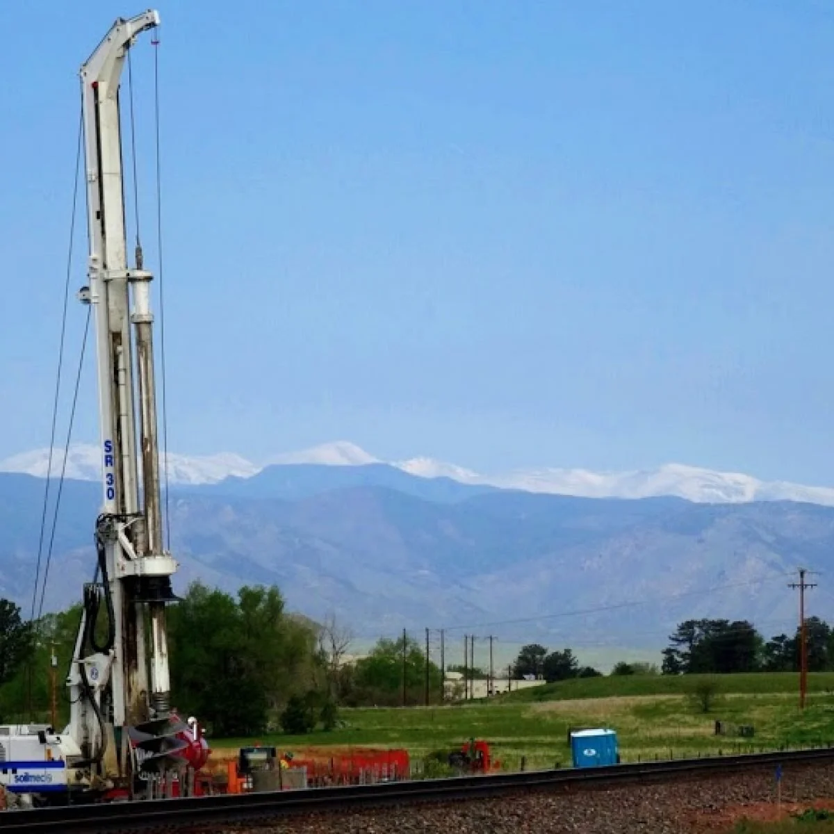Construction crane near railroad tracks with mountains and snow-capped peaks in the background.