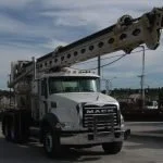 A large white crane truck with an extended boom on a street under a cloudy sky.