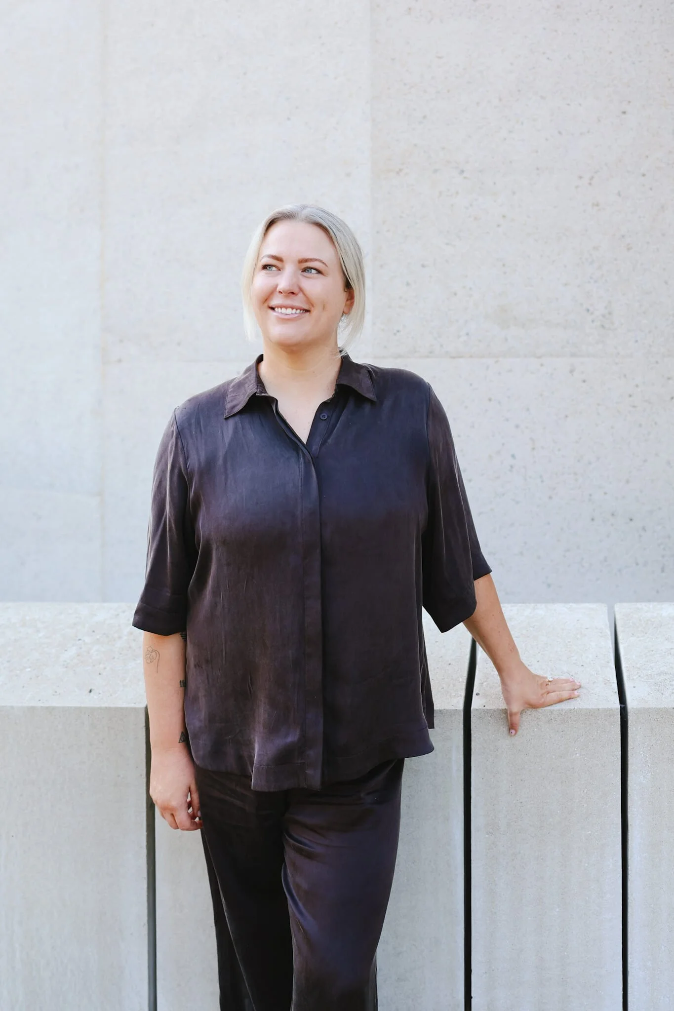 Renee of Love Better, standing wearing a dark, loose-fitting shirt and pants, standing outdoors against a light-colored concrete wall.