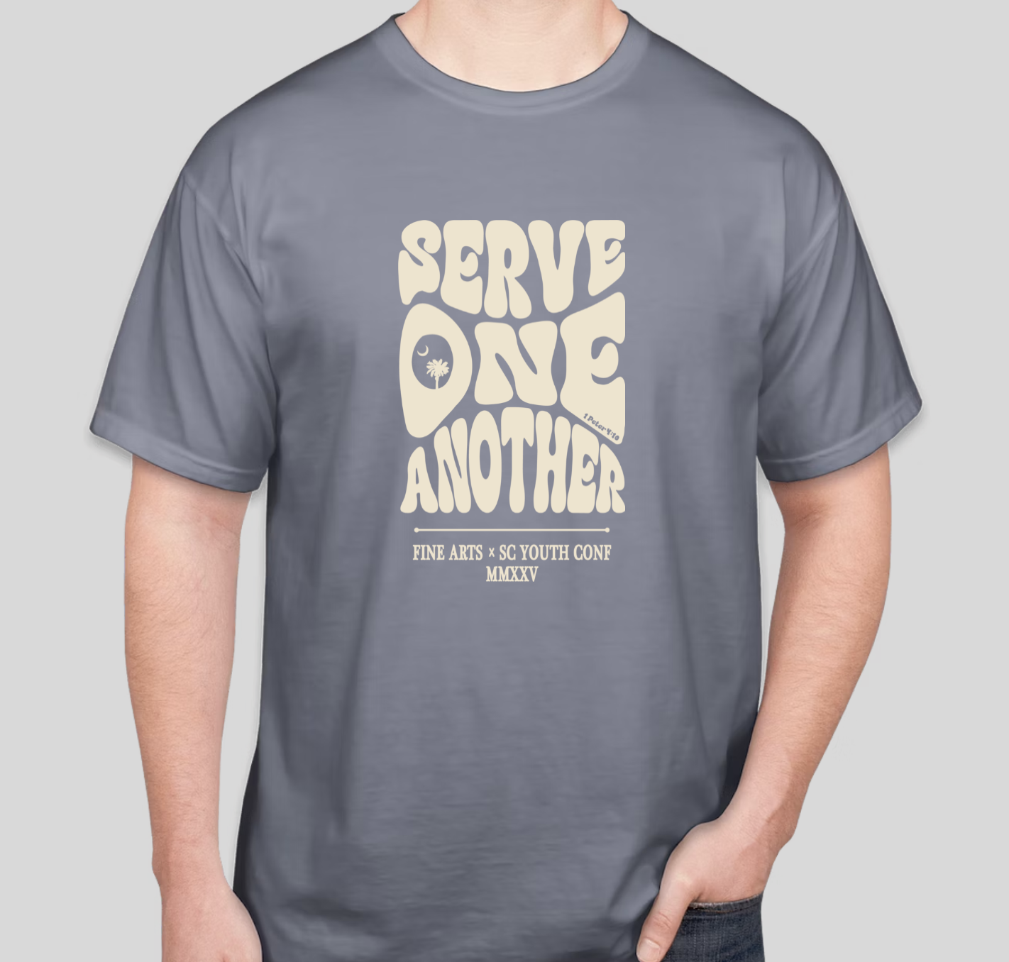 Gray T-shirt with the phrase 'Serve one another' in large, rounded letters and a small palm tree and moon graphic, along with text about an art conference.