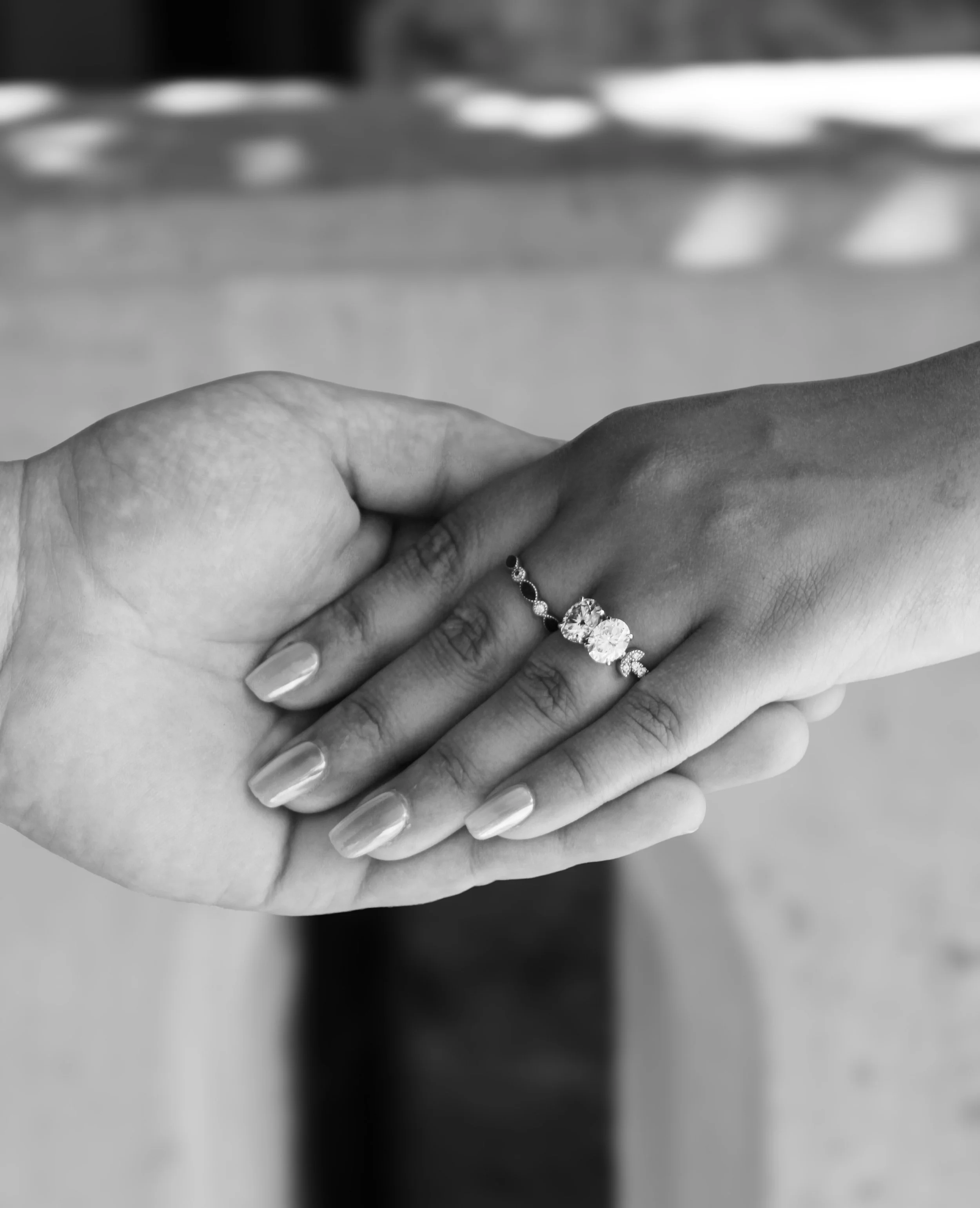 A close-up of two hands with one wearing a ring, in black-and-white, with a blurred background.