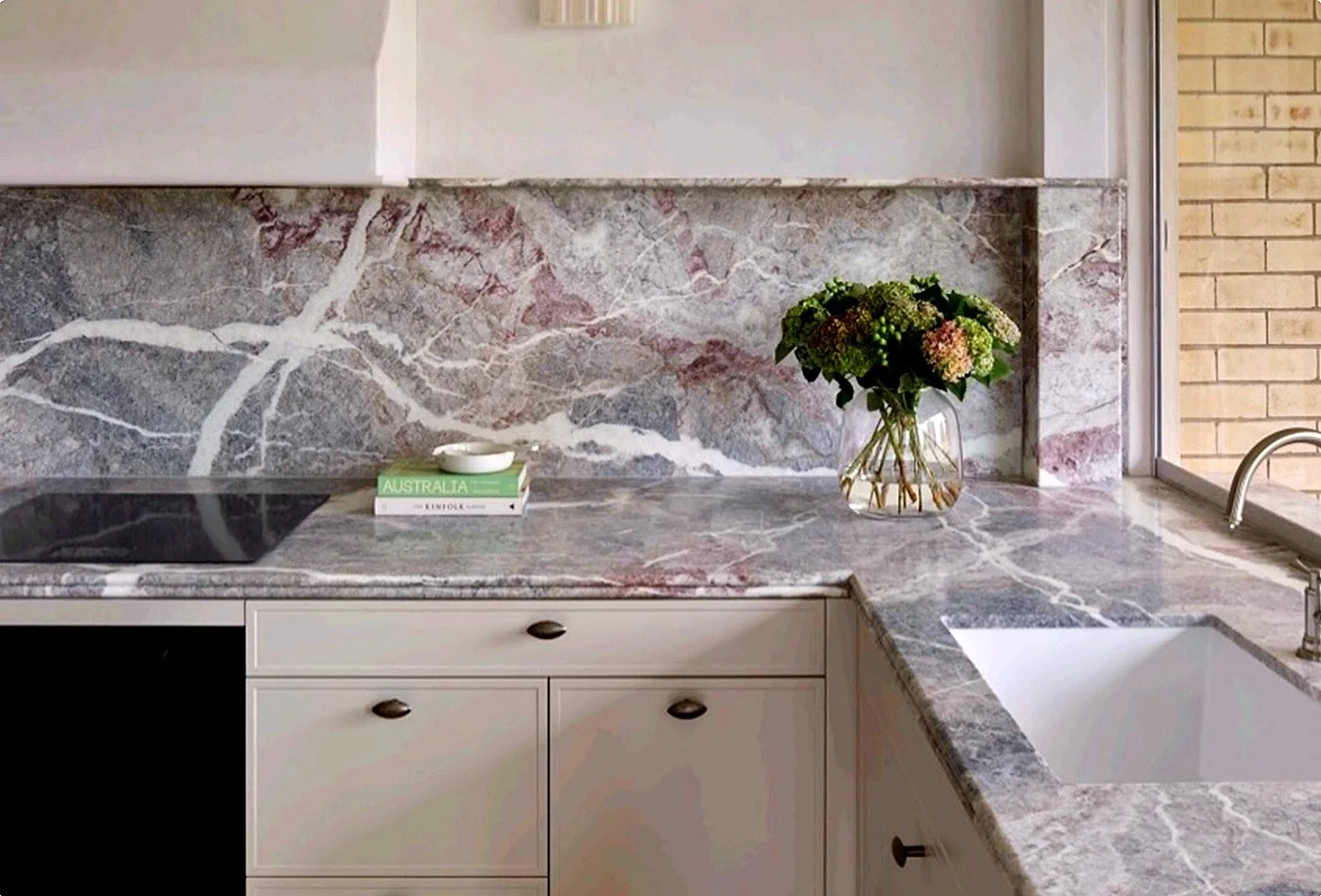 A kitchen countertop with a marble surface, a vase with flowers, a stack of books, and a window.