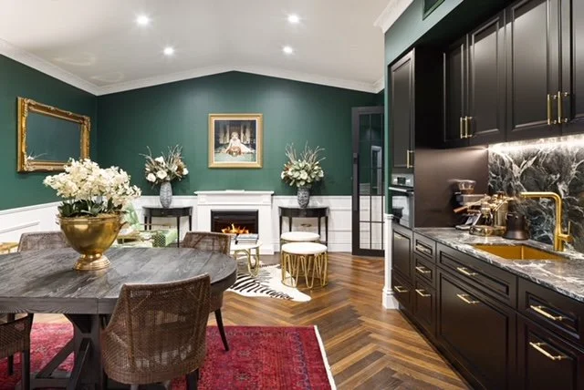 Modern dining and kitchen area with dark cabinetry, marble countertops, green walls, hardwood floors, and elegant decor including flower arrangements and framed artwork.
