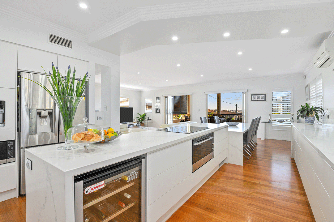 Bright, modern kitchen with white cabinets, marble island, stainless steel appliances, hardwood flooring, and large windows with view of outdoor landscape.