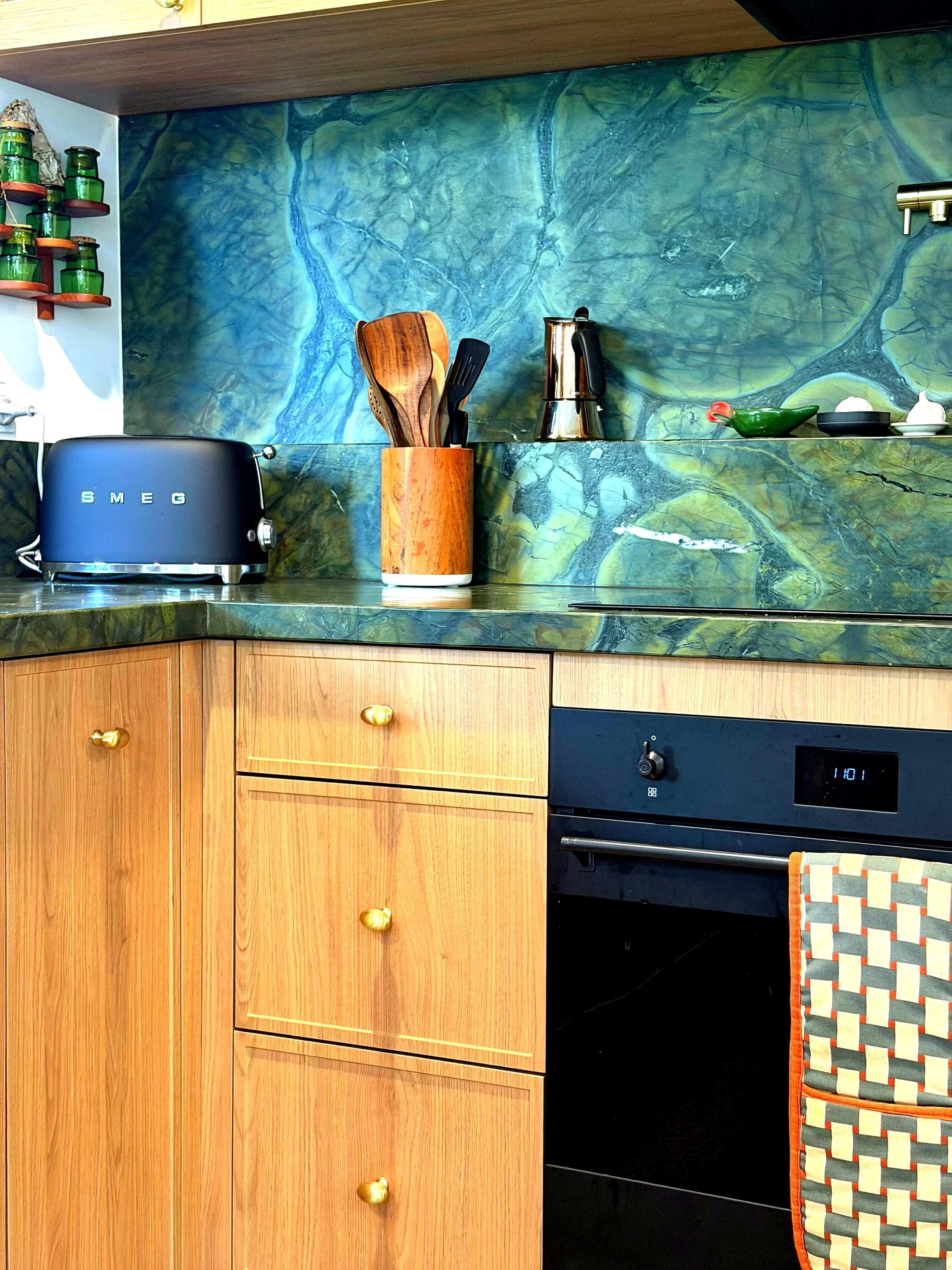 A kitchen countertop with a black SMEG toaster, wooden multi-purpose utensils in a cylindrical container, a silver electric kettle, and decorative items including a small green ceramic dish shaped like a bird, a black dish with a white lid, and a whi