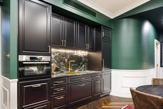 Kitchen with dark cabinets, marble backsplash, gold fixtures, green walls, and a dining table with chairs.