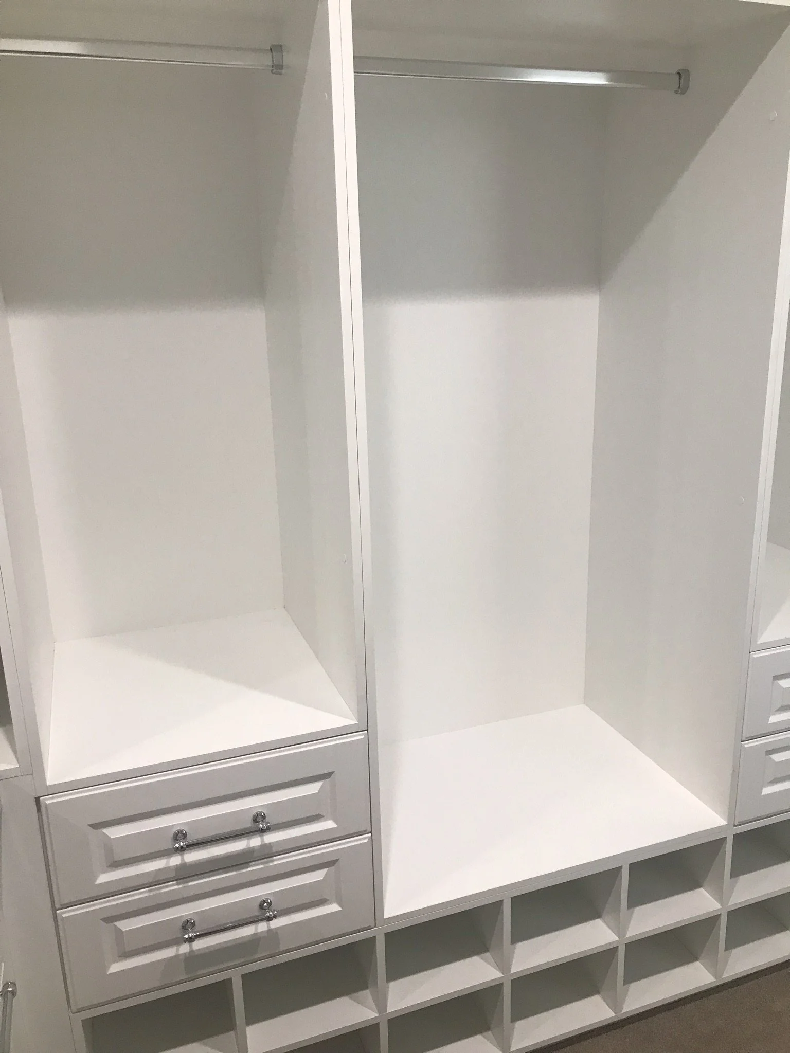 Empty white closet with multiple compartments, drawers, and small cubbies.