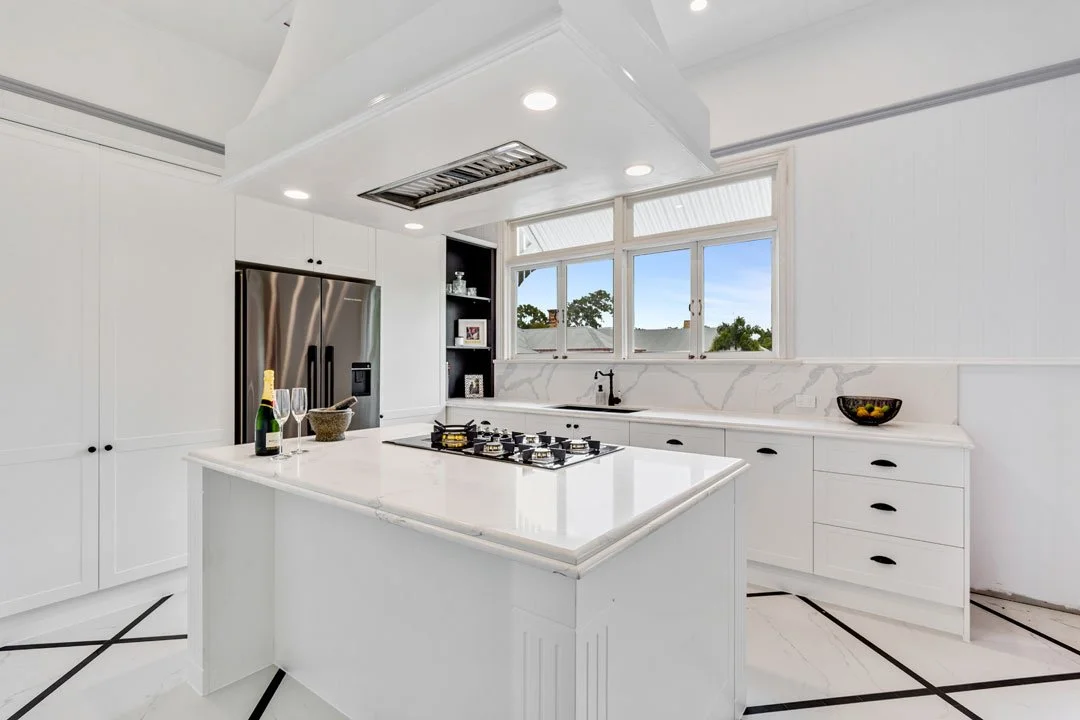 White kitchen with marble countertops, a central island, a window with a view outside, and stainless steel appliances.