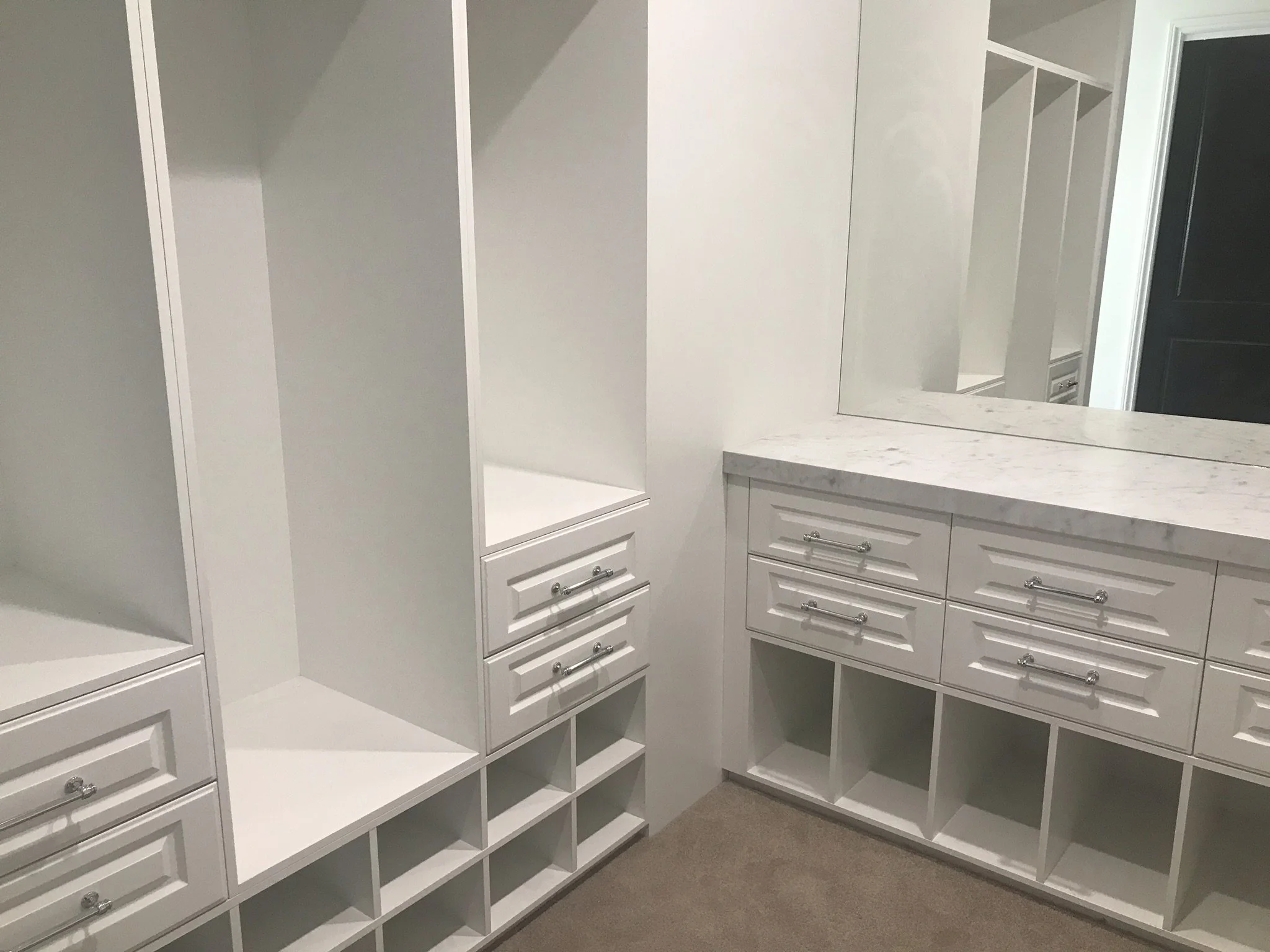 Empty white closet with numerous open shelves, drawers, and a large mirror on one wall.