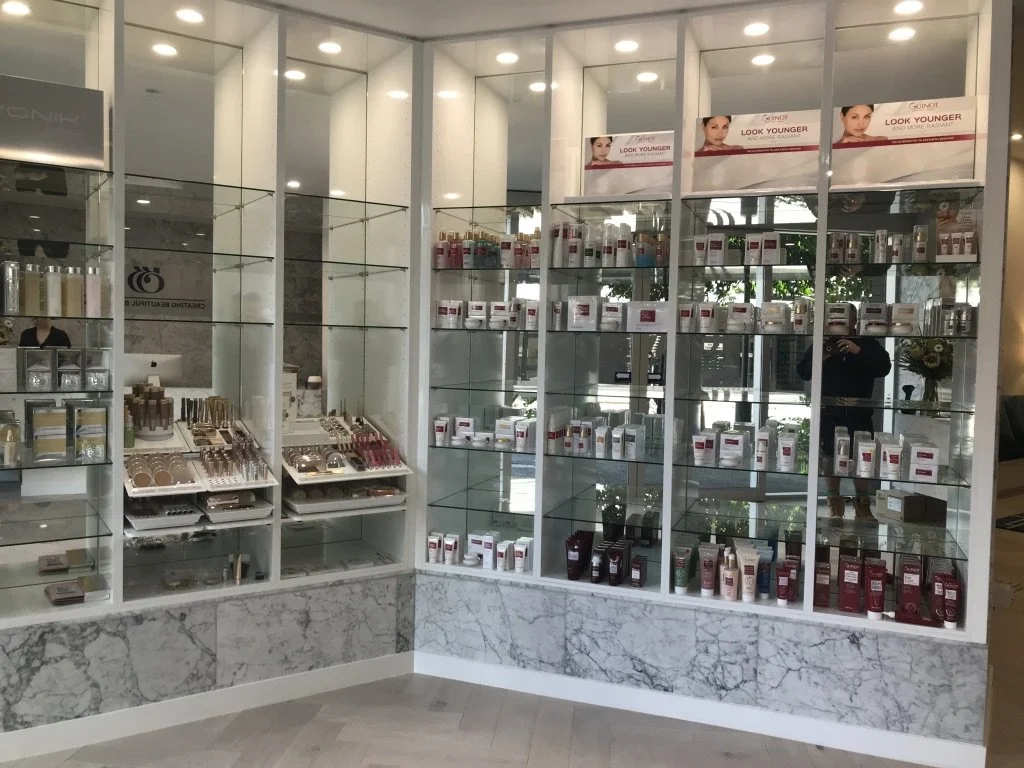 Display shelf with skincare products, cosmetics, and beauty items in a store with glass shelves and marble accents.