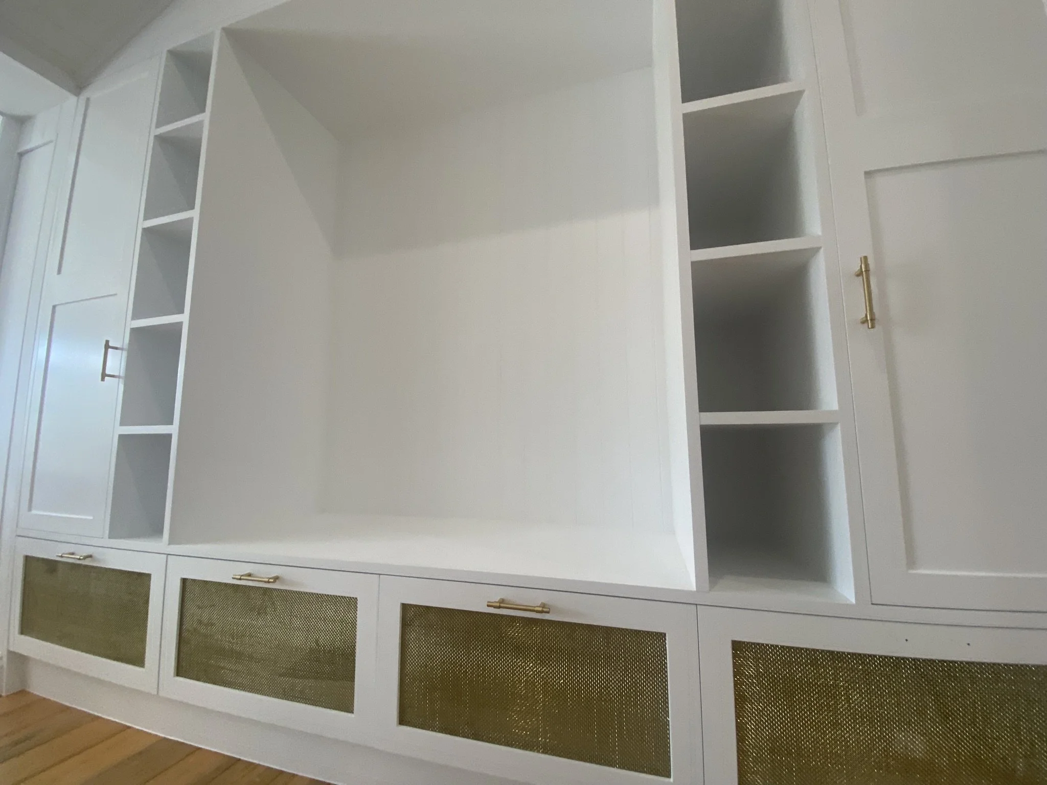 White built-in cabinet with open shelves and gold handles against a wall with wooden flooring.