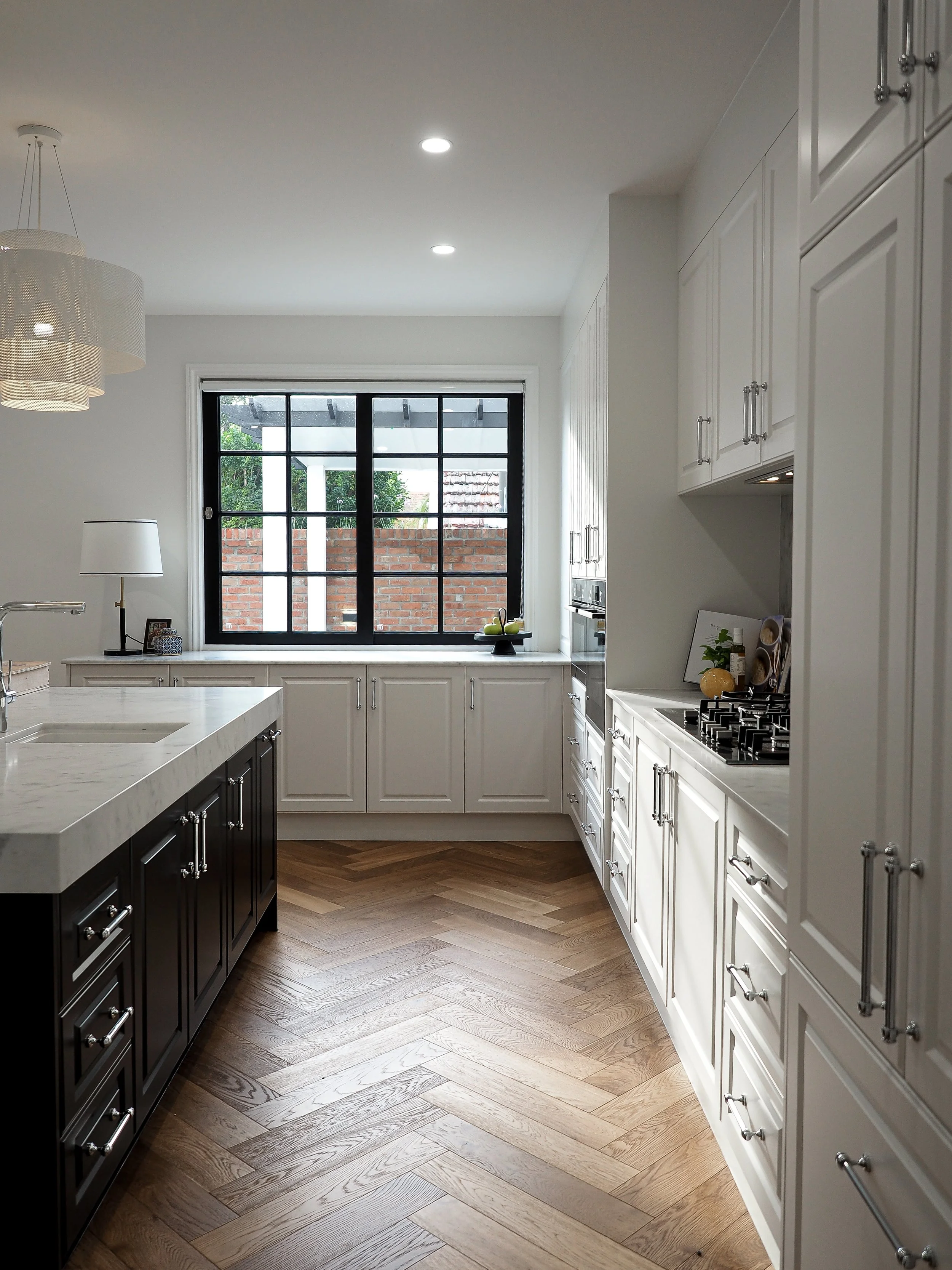 Modern kitchen with white and black cabinetry, wooden flooring, large window, and small decorative items on the countertops.