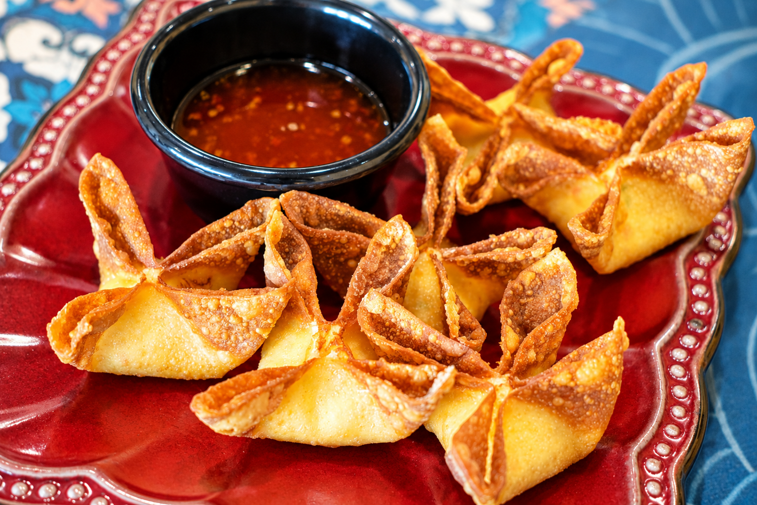 Fried wontons with dipping sauce on a decorative red plate.